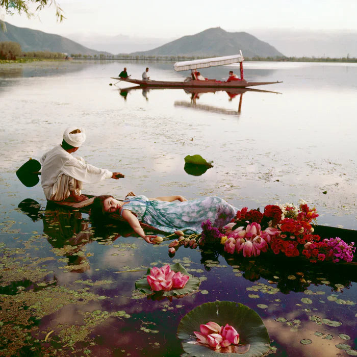 Anne Gunning is photographed floating in a cotton mousseline dress by Atrima on India's Dal Lake for a British Vogue shoot in 1956. In the background, model Barbara Mullen sits in a boat rowed by locals across the water.