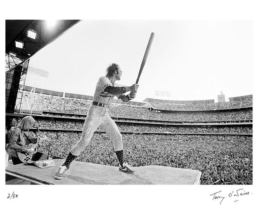 Elton John peforming with a baseball bat, 1975 — Limited Edition Print - Terry O'Neill
